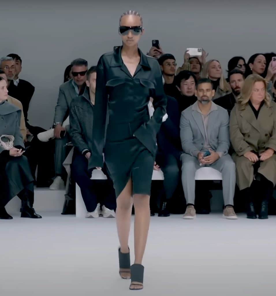 model wearing an all black dress with satin lapels and black shoes/sunglasses